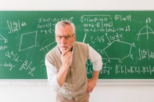 elder professor in classroom looking at camera with question